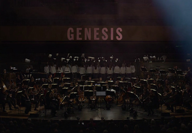 Utdrag ur filmen Genesis. Stor orkester och upplyst i bakgrunden med tetxen Genesis. Fotografi.