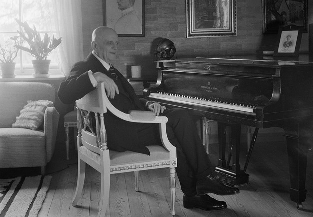 Old man sitting by the piano in his home. Black and white photography.